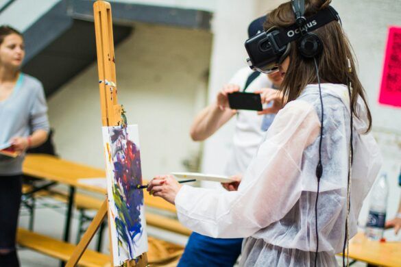Garota jovem faz pintura colorida em uma tela sobre cavalete, enquanto utiliza óculos de realidade virtual. Dessa forma, associando o aprendizado às tendências e inovações