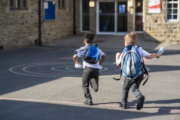 Dois garotos correm em direção à escola após o retorno das férias escolares.