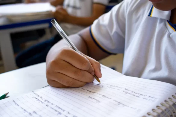 Criança em sala de aula escreve em caderno pautado.