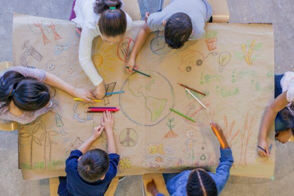 Imagem vista de cima de crianças trabalhando em conjunto para compor um desenho sobre educação ambiental.